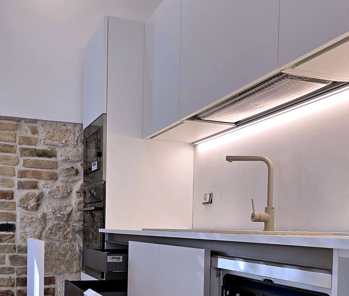 Cucina moderna con parete in pietra e luce sotto i pensili